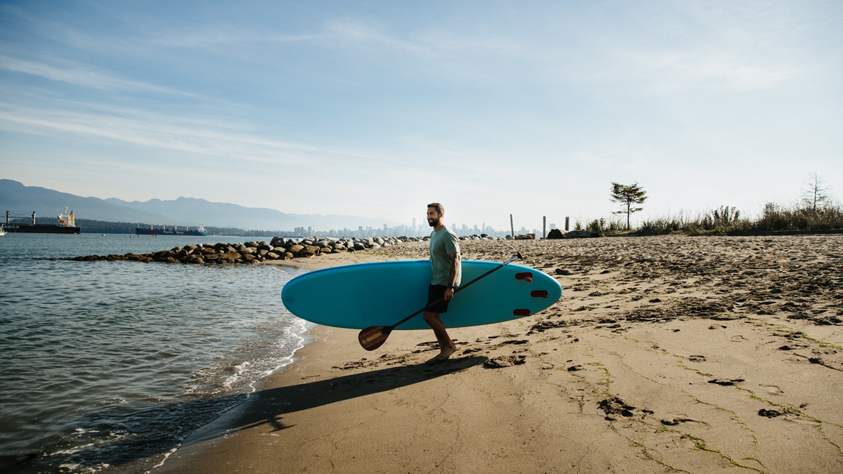 A man carries a paddleboard to the beach in Vancouver